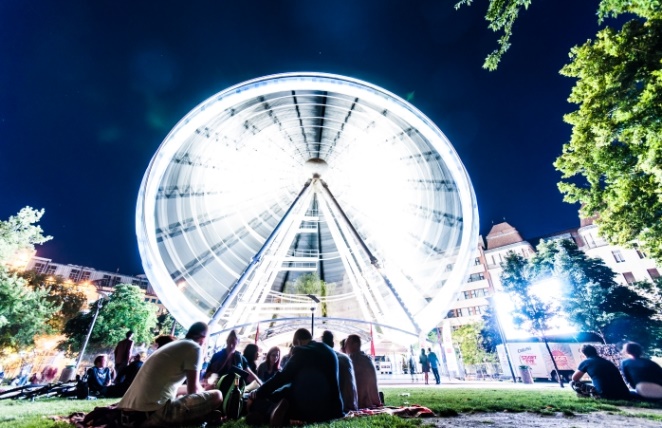 friends gather in a budapest park to chat, while a ferris wheel spins the background.