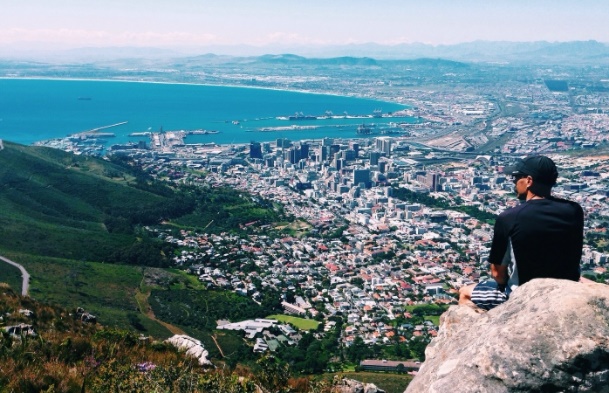 a man sits atop of a rock looking out over the cape town coastline.